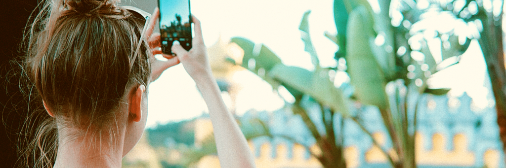 A girl taking pictures with her phone of some banana trees